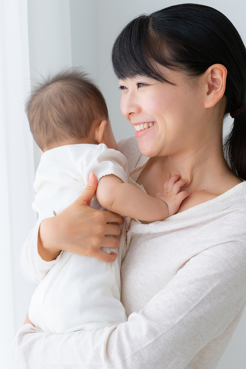 Smiling Asian mother holding infant standing beside window