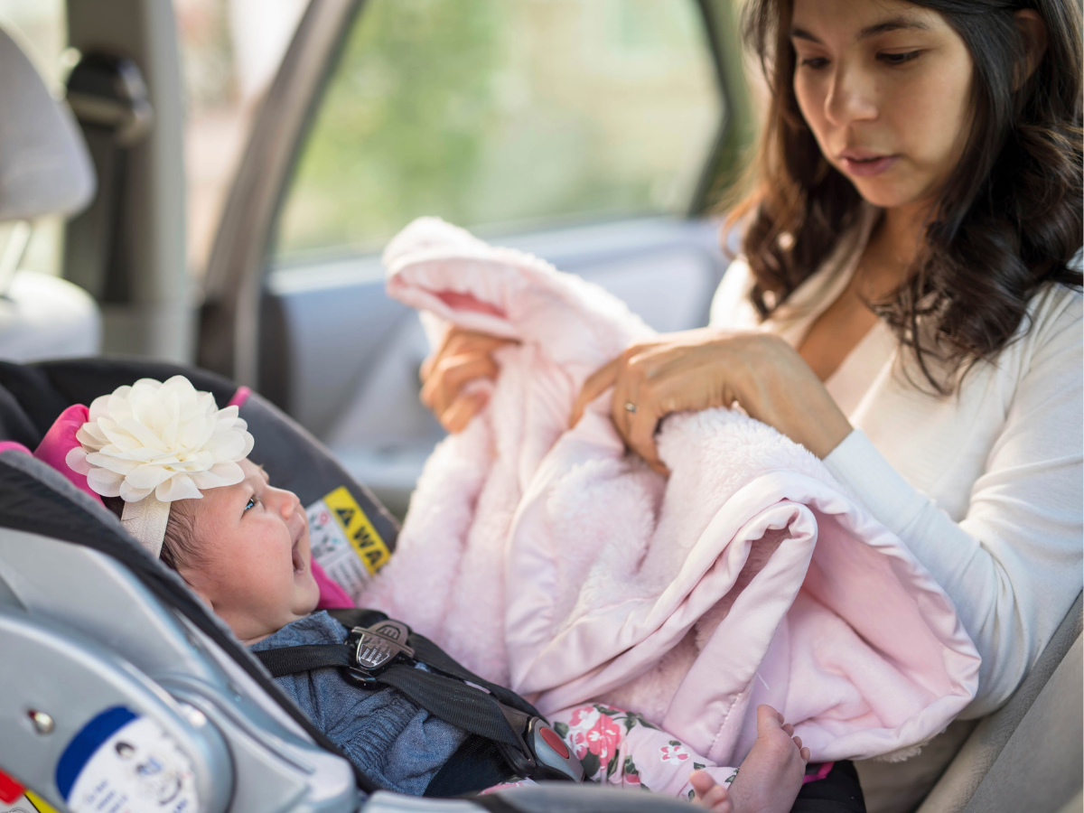 baby in car seat being tucked in by mom with pink blanket